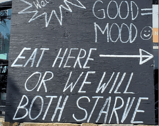 Restaurant sign saying "Eat here or we will both starve"