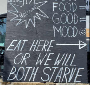 Sign outside restaurant that says "Eat here or we will both starve"